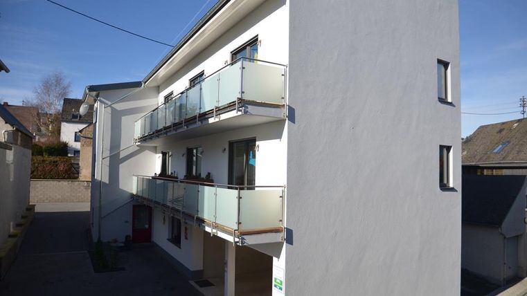 A modern building with three balconies and a bright facade. It is located in a quiet environment and has a clear blue sky in the background.