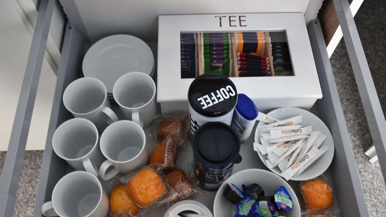 A drawer full of coffee cups, tea, and snacks. Beneath are muffins and cream portions.