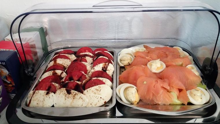 A buffet with two different dishes. On the left side are tomatoes and mozzarella, on the right smoked salmon with eggs.