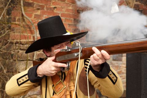 A man in historical clothing aims with a historical rifle, a so-called musket.
