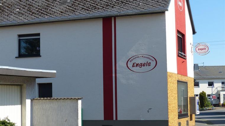 Ein zweigeschossiges Gebäude mit einer weißen und roten Fassade. An der Wand ist das Schild "Engels" angebracht.