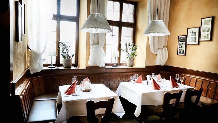 Ein gemütliches Restaurant mit hellen Fenstern und eleganten Tischen. Die Tische sind mit weißen Tischtüchern und roten Servietten dekoriert.