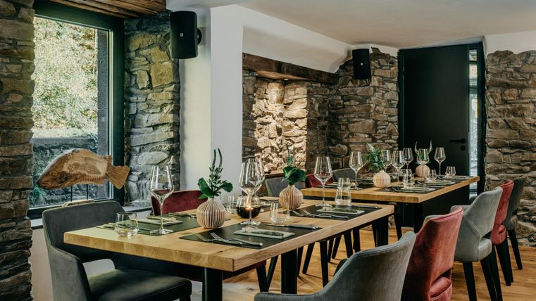 Ein modernes Restaurant mit Holztischen und stilvollen Stühlen. Große Fenster lassen viel Licht hereinfliessen und bieten einen Blick auf die natürliche Umgebung.