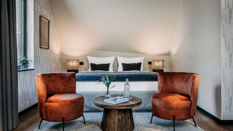 Ein modernes Schlafzimmer mit einem komfortablen Bett und zwei stilvollen Sesseln. Der Raum ist hell und elegant eingerichtet, ideal für Entspannung.