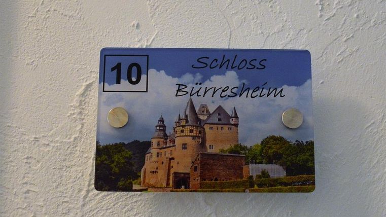 A sign with the inscription "Bürresheim Castle" and the number 10. The picture shows a beautiful castle surrounded by trees and a blue sky.