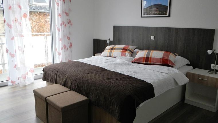 A modern bedroom with a double bed and comfortable pillows. The windows are decorated with curtains and there is a small table.