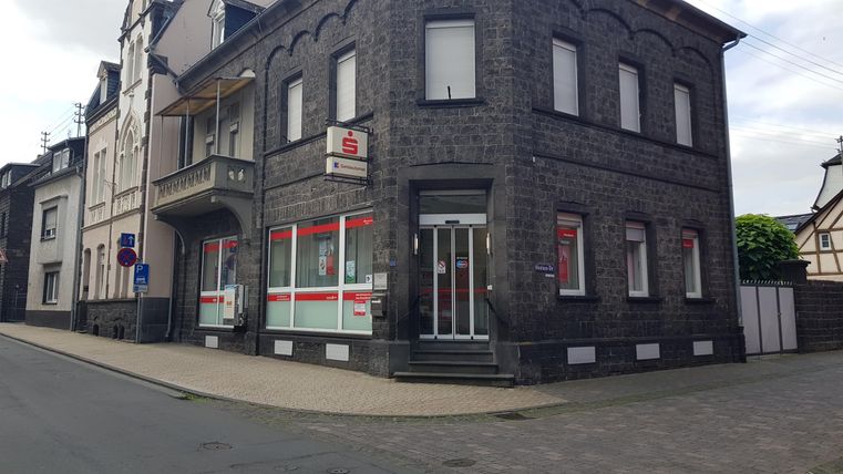 Ein graues Gebäude an einer Straßenecke mit großen Fenstern. Vor dem Gebäude befindet sich ein kleiner Gehweg und Straßenschilder.