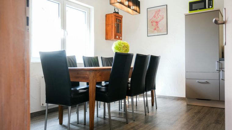 A bright dining area with a large wooden table and black chairs. The walls are friendly designed, and a refrigerator is in the corner.