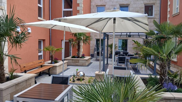 A cozy courtyard with palm trees and sun umbrellas. There are tables and chairs inviting you to relax.