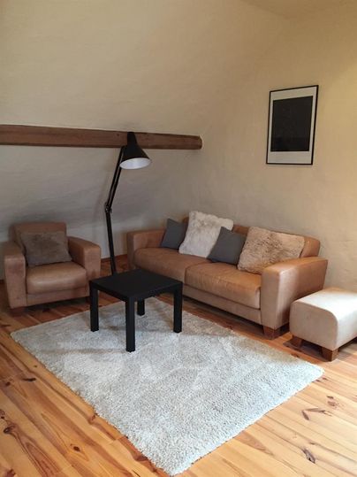 A cozy living space with a beige sofa and an armchair. The room has a wooden floor and a modern floor lamp.