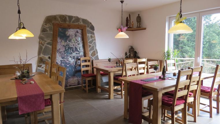 Ein gemütliches Restaurant mit Holztischen und Stühlen. Die Wände sind hell und es gibt große Fenster, die viel Licht hereinlassen.