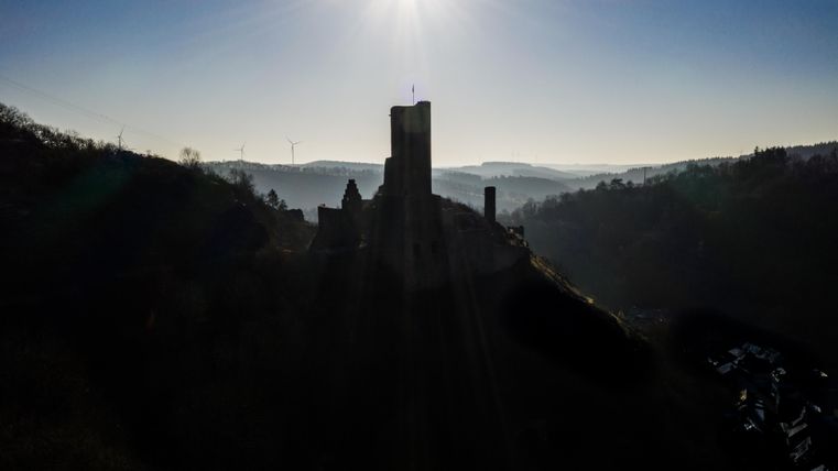 An impressive castle on a hill, surrounded by gentle hills and the morning glow. The sky is clear and radiant.