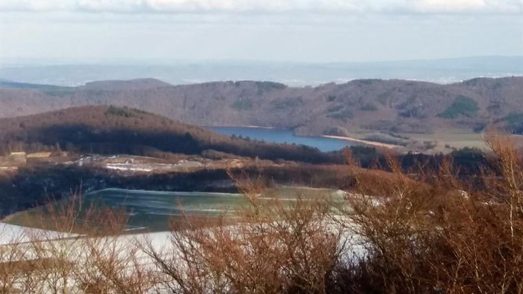 A picturesque landscape with gentle hills and a tranquil body of water. The sky is cloudy and nature is in a winter look.