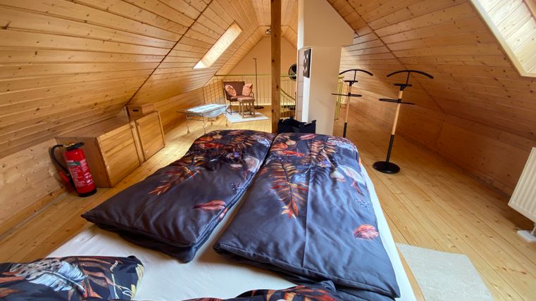 Ein gemütliches Schlafzimmer im Dachgeschoss mit Holzwänden und einem großen Fenster. Das Bett ist mit bunten Bettdecken und Kissen dekoriert.