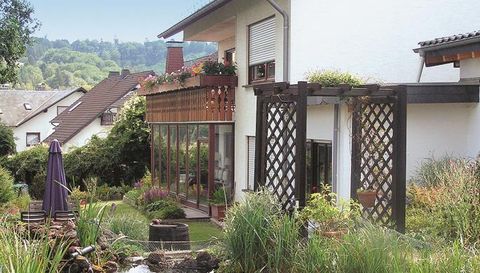 A modern house with a beautiful garden and a green lawn. There is a terrace with flowers and privacy screen.