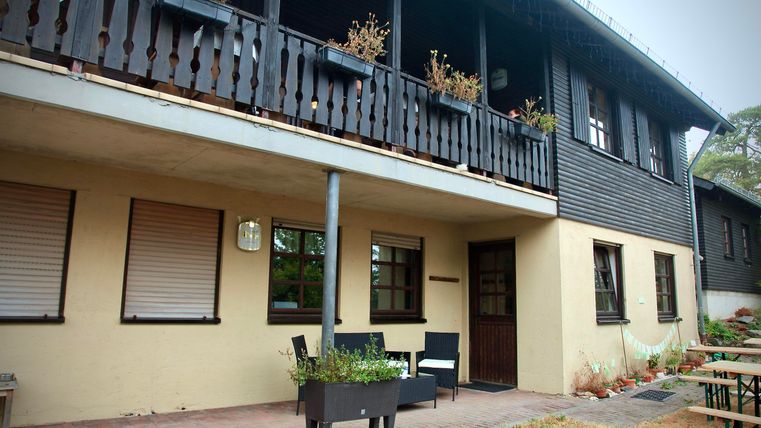 Ein modernes Haus mit einem Balkon und einigen Pflanzen. Vor dem Haus stehen Gartenmöbel für einen gemütlichen Aufenthalt.