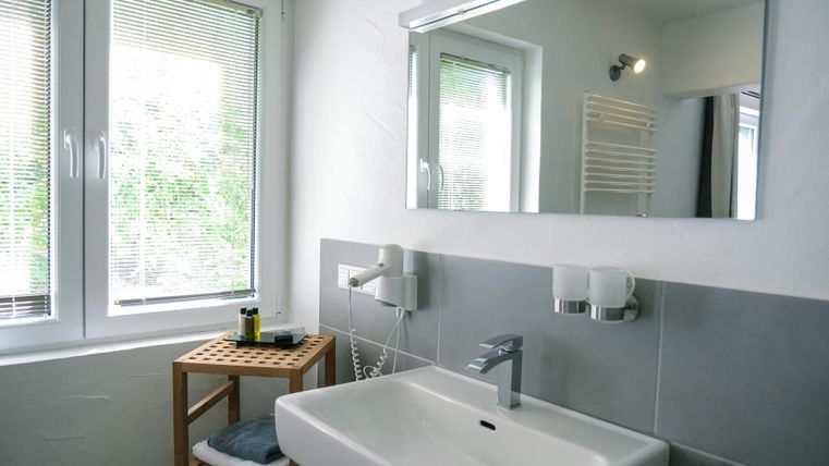 A modern bathroom with a large mirror and a sink. There is a wooden shelf with towels and toiletries.