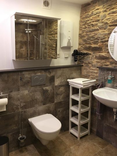 Ein modernes Badezimmer mit Steinwänden und eleganten Fliesen. Es enthält eine Dusche, ein Waschbecken und praktische Ablagemöglichkeiten.