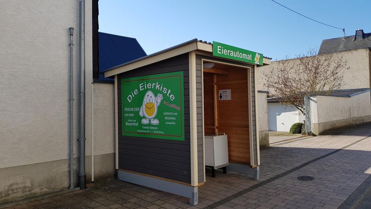 A small sales stand with a green sign offering eggs. The stand is located on a quiet street and is easily visible.