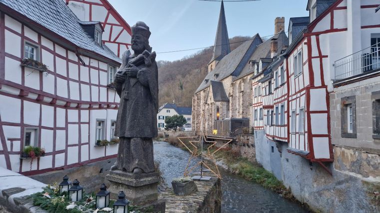 Eine malerische Stadt mit traditionellen Fachwerkhäusern und einem kleinen Fluss. Im Vordergrund steht eine Statue, die die Umgebung bereichert.