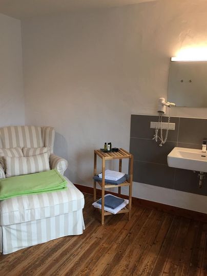 A cozy room with a comfortable armchair and a small wooden shelf. On the wall, there is a modern sink with a mirror.