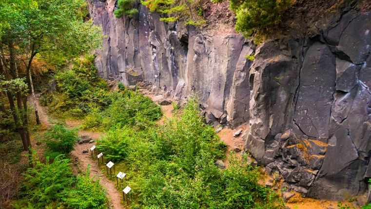 Eine beeindruckende Schlucht mit steilen Felsen und üppiger Vegetation. Wanderwege und Informationsschilder laden zur Erkundung der Umgebung ein.