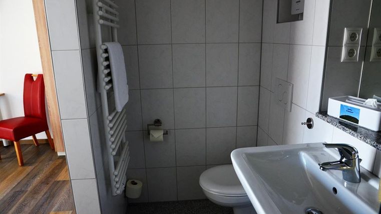 A modern bathroom with tiled walls and clean lines. In the foreground, there is a sink and a toilet, while a towel rack hangs on the wall.