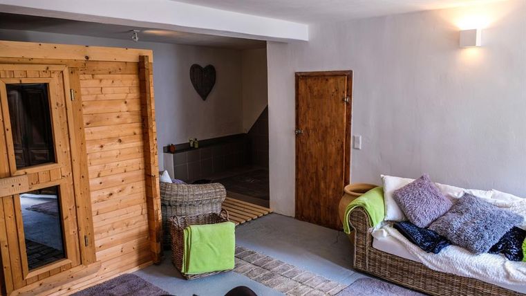 A bright room with a cozy seating area and a wooden sauna area. The walls are kept neutral, and there are decorative elements that create a relaxed atmosphere.