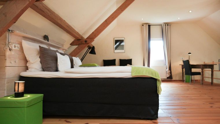 A modern bedroom with a large bed and wooden floor. The room has a bright atmosphere and is furnished with a table and chairs.