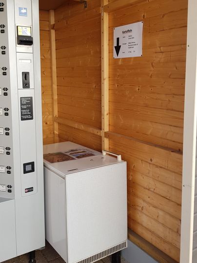 A small room with a vending machine and a refrigerator. The walls are made of wood and a sign is installed.