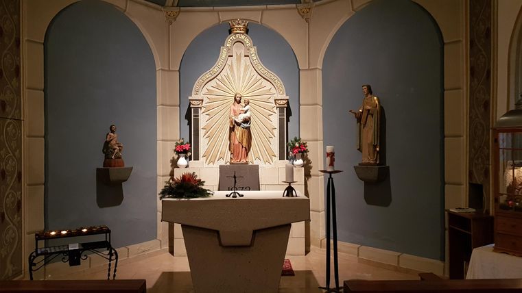 A small chapel with an altar and a statue. The walls are painted blue and there are decorative figures.