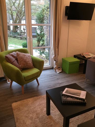 A cozy living room with a green armchair and a black table. Through the windows, you can see a beautiful garden.