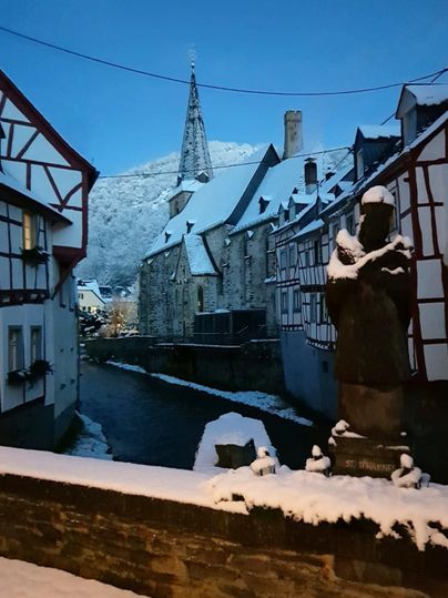 Ein malerisches Dorf im Schnee mit historischen Fachwerkhäusern. Im Hintergrund ragt ein Kirchturm gegen den klaren, blauen Himmel.