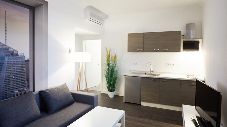 A modern living room with a kitchenette and a couch. The room is bright and cheerfully designed.