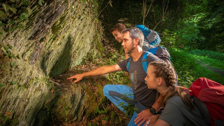 Three people look at a rock face in the forest.