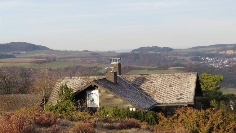 Ein gemütliches Haus auf einem Hügel mit einer schönen Landschaft im Hintergrund. Die sanften Hügel und das klare Wetter verleihen der Szene eine friedliche Atmosphäre.