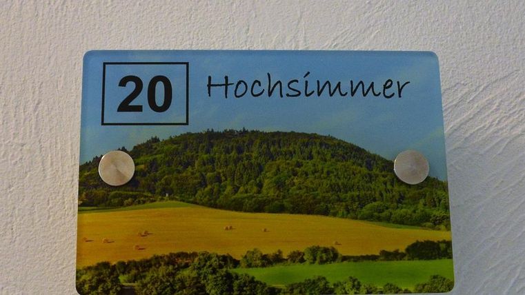 A sign with the number 20 and the inscription "Hochsimmer". In the background, there is a green landscape with hills and fields.
