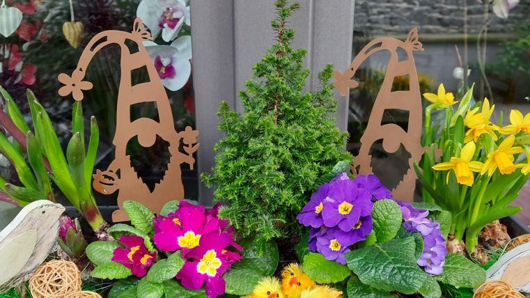 A colorful flower arrangement with various plants and colorful blooms. Two creative figures in the form of gnomes add a cheerful accent to the arrangement.