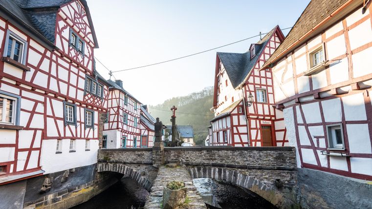 Eine malerische Brücke verbindet historische, Fachwerkhäuser in einer ruhigen Landschaft. Der Himmel ist klar und die Umgebung strahlt Gemütlichkeit aus.