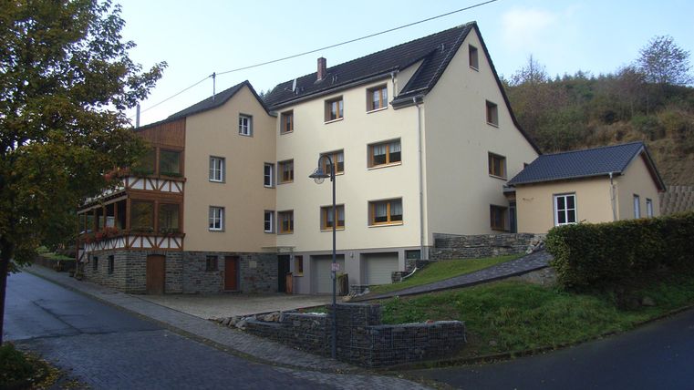 Ein großes, mehrstöckiges Gebäude in einer ländlichen Umgebung. Es ist teilweise umgeben von Bäumen und einer gepflasterten Straße.