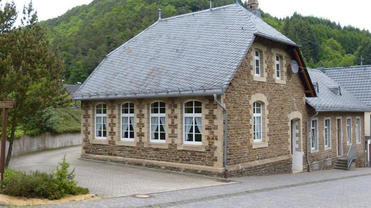 Ein hübsches, traditionelles Gebäude aus Stein mit einem Satteldach. Umgeben von Bäumen und einem klaren Gehweg.