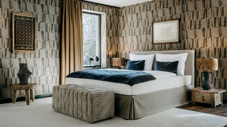 Ein modernes Schlafzimmer mit einem großen Bett und stilvollen Dekorationen. Die Wände sind mit einem interessanten Muster gestaltet und das Fenster lässt viel Licht herein.