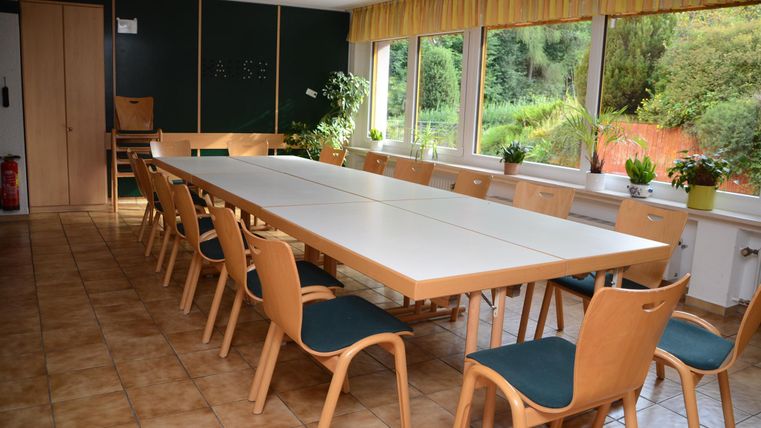 Ein heller Besprechungsraum mit einem langen Tisch und vielen Stühlen. Große Fenster bieten einen Blick ins Grüne.