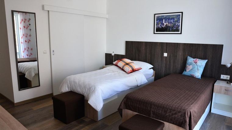 A bright bedroom with two beds and a minimalist design. A picture hangs on the wall, and there is a large mirror that expands the space.