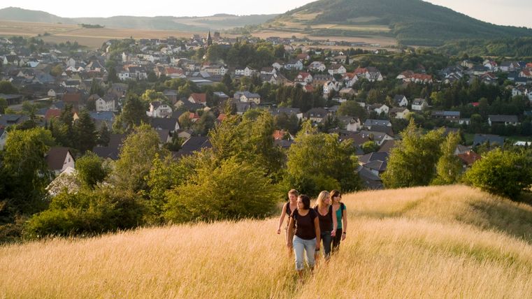 Group of people walking through a field with a view of Ettringen in the background.