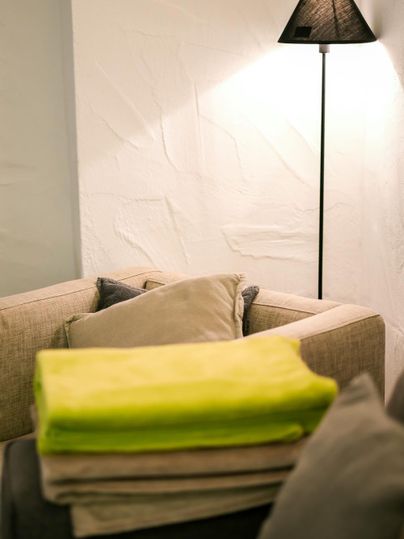 A cozy living room with a sofa and a floor lamp. Several blankets are on the table, including a bright yellow one.