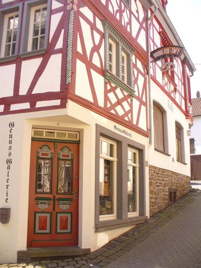 Ein charmantes Fachwerkhaus mit einer bunten Haustür und einem einladenden Café-Schild. Die Fassade zeigt schöne, traditionelle architektonische Details.