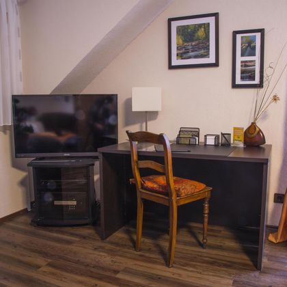 Ein gemütliches Arbeitszimmer mit einem Schreibtisch und einem Stuhl. Ein Fernseher und dekorative Bilder ergänzen den Raum.