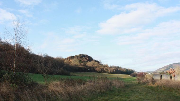 A tranquil landscape with green meadows and gentle hills. The sky is blue with some clouds.