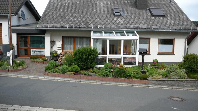 Ein gemütliches Einfamilienhaus mit einem Garten und einer Veranda. Der Vorgarten ist grün und einladend gestaltet.